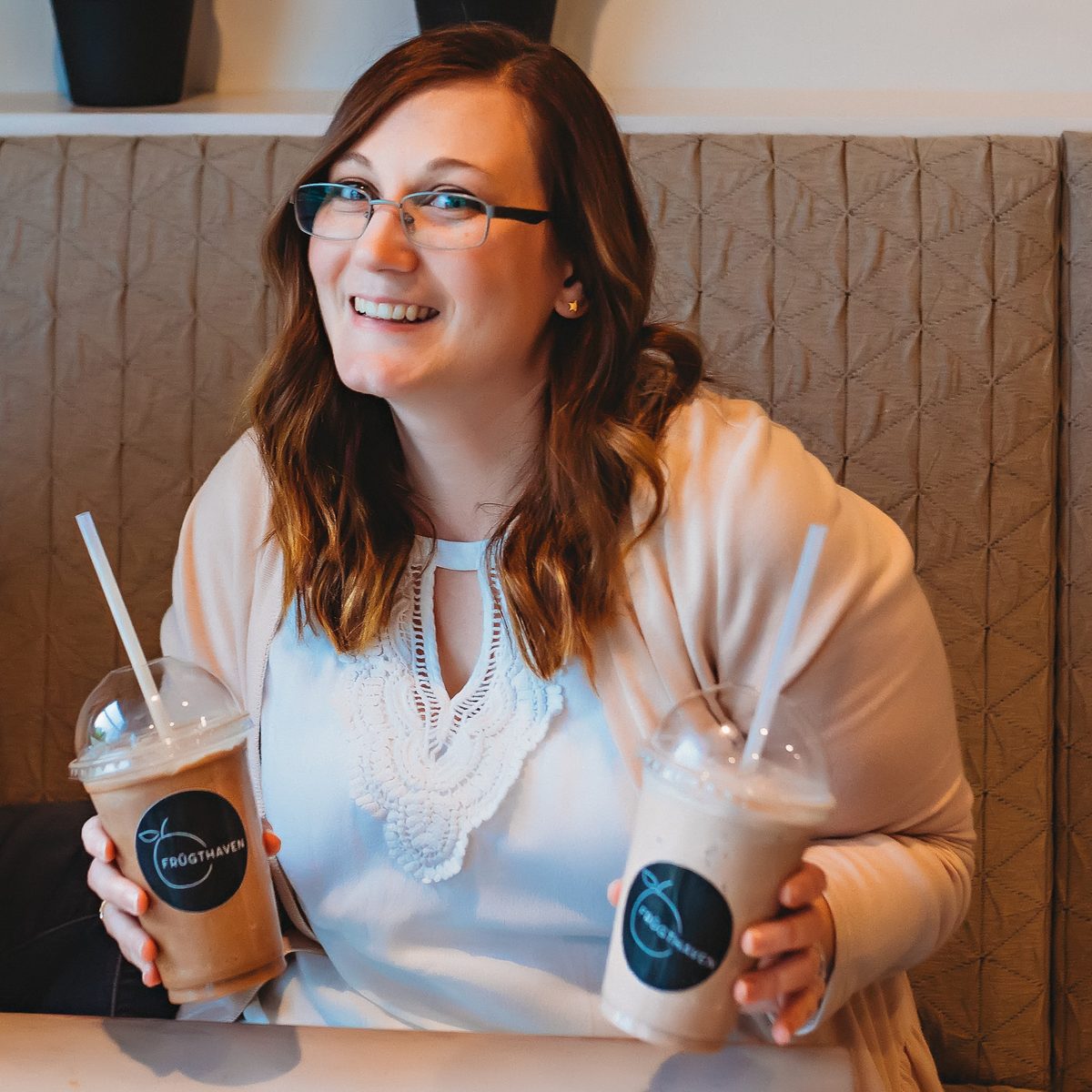 Ariel smiling over her shoulder in a booth, holding two iced coffee drinks with straws.