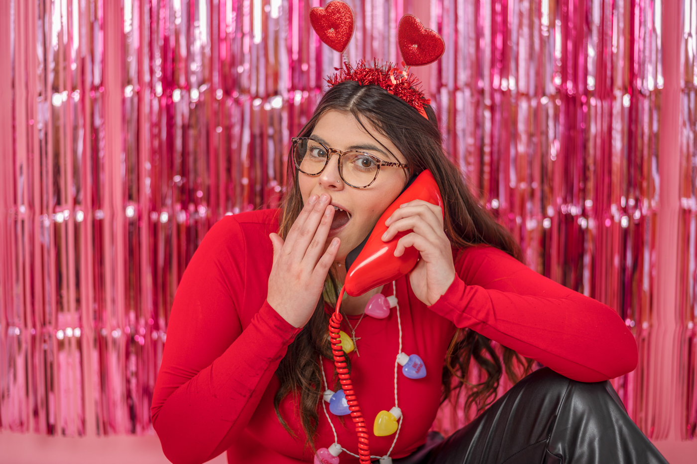 high school girl posing with lip shaped phone in front of pink fringe backdrop for photo shoot