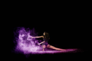 Dancer in motion on a dark background, creating a cloud of purple flour powder around them.
